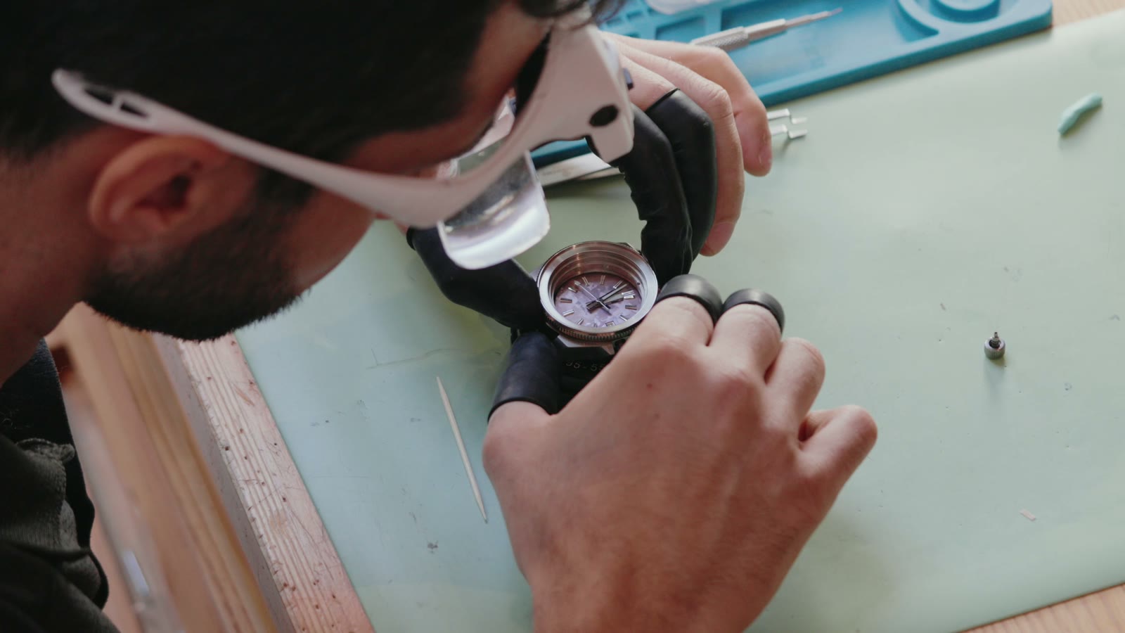 Namir assembling a watch at his workbench while wearing a watchmaking loupe